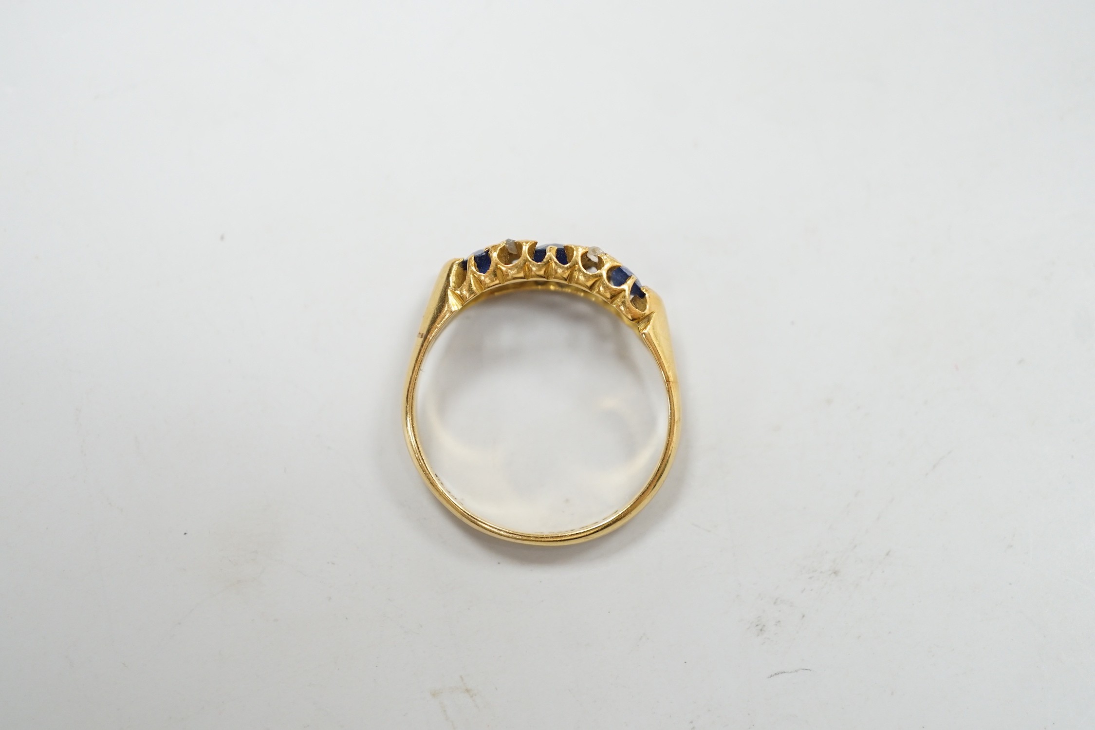 An Edwardian 18ct gold and graduated three stone sapphire set half hoop ring, with four stone rose cut diamond chip spacers, hallmarked for Birmingham, 1906, size P/Q, gross weight 3.2 grams.